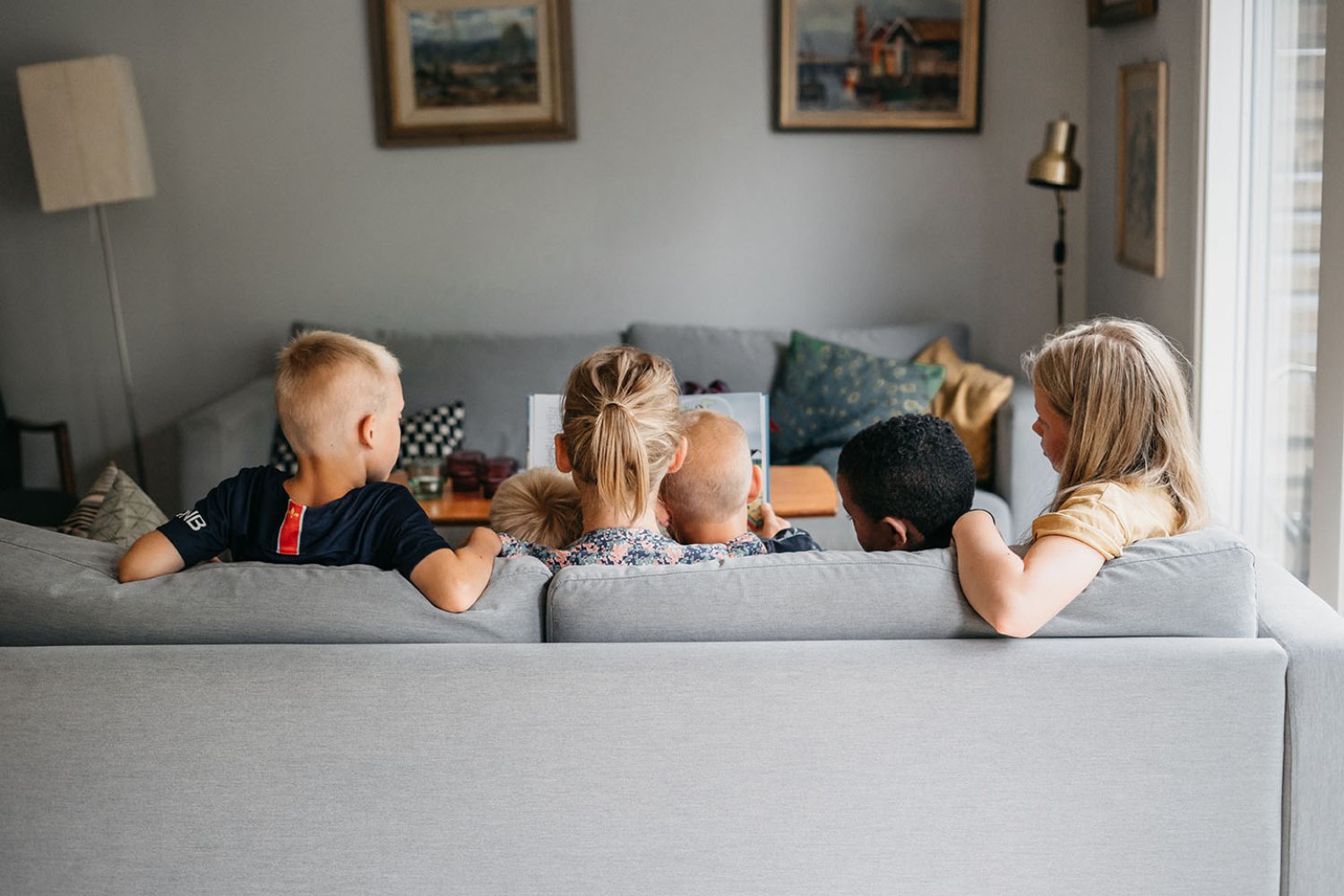 En mamma och fyra barn sitter i en soffa och läser en bok.