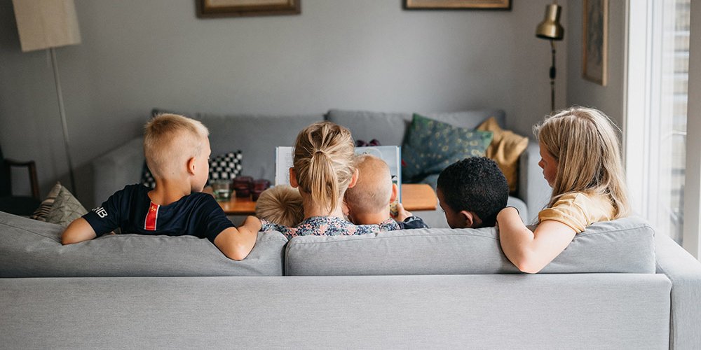 En mamma och fyra barn sitter i en soffa och läser en bok.
