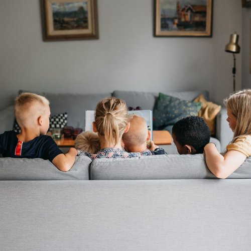 En mamma och fyra barn sitter i en soffa och läser en bok.