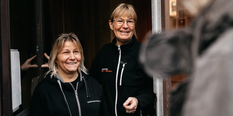 Två medarbetare på Räddningsmissionens frukostcafé välkomnar en gäst i dörren.